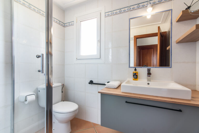 Helles Badezimmer mit Glasdusche, WC, Waschbecken auf Holzplatte, Spiegel und Fenster im Ferienhaus in Portocolom auf Mallorca